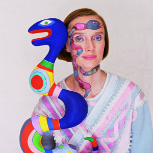 Niki de Saint Phalle holds a snake sculpture while wearing a face painting of a snake. --- Image by © Norman Parkinson/Corbis