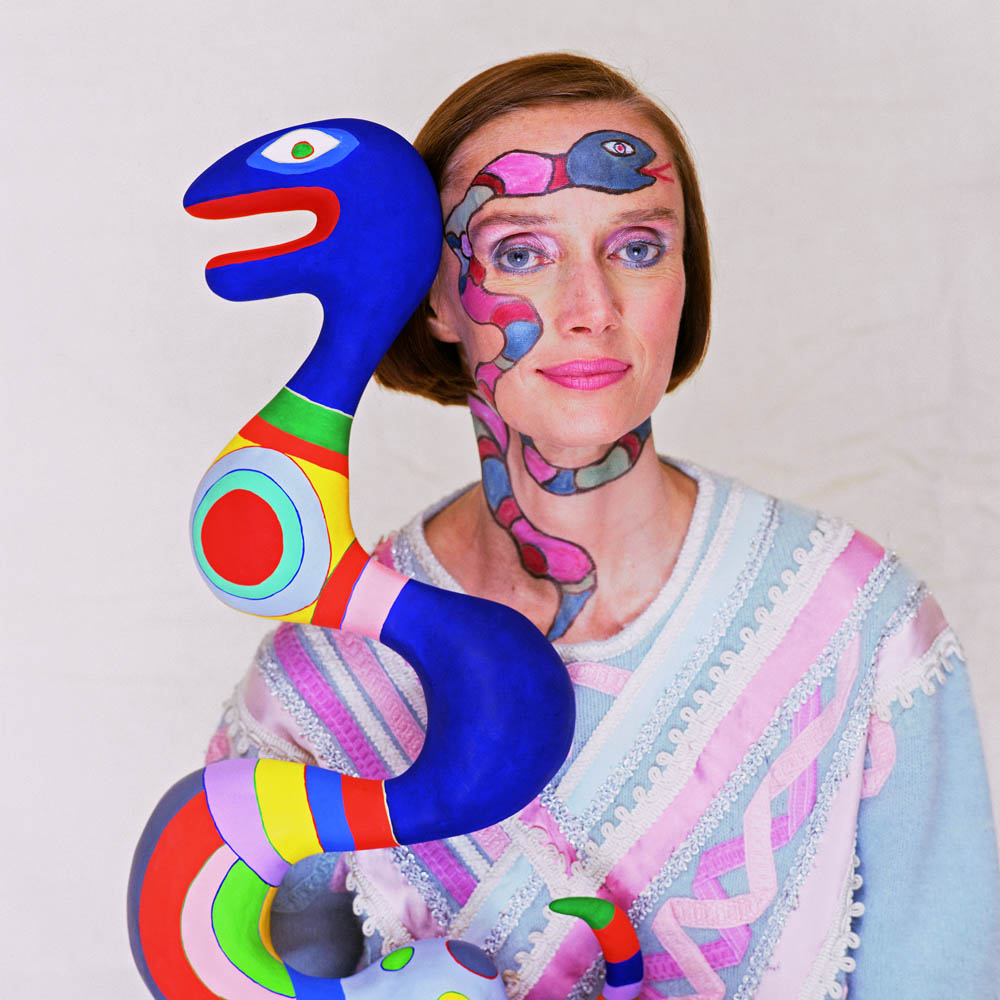 Niki de Saint Phalle holds a snake sculpture while wearing a face painting of a snake. --- Image by © Norman Parkinson/Corbis